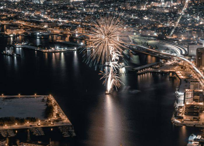 Fireworks being set off from a boat in Japan. Behind it, a city stretches out.